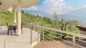A terrace with a curved railing, a table with chairs, and a view of a mountainous landscape. - Beautiful apartment for 5 guests with WIFI, TV, patio and panoramic view (Riva Del Garda)