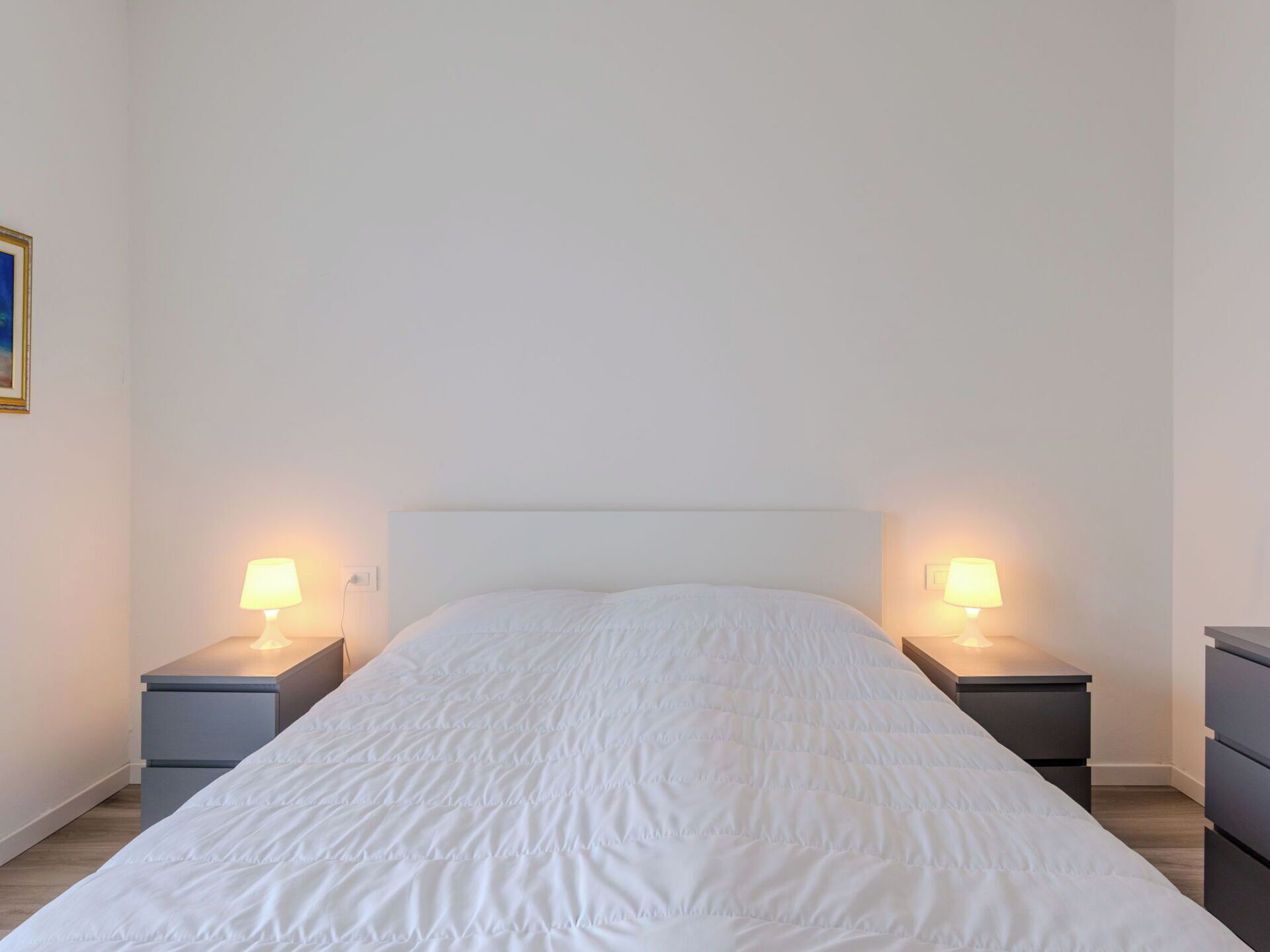 A single bed with a white headboard in a room with two bedside tables, each with a lamp.