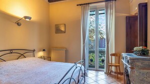 Une chambre à coucher avec un lit, un radiateur, une fenêtre avec des rideaux, une chaise et une petite table ornée de fleurs.