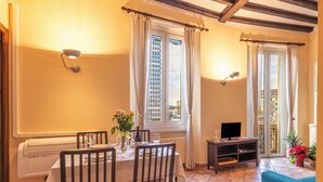 Un coin repas avec une table dressée pour quatre personnes, un téléviseur posé sur un meuble et une fenêtre avec des rideaux.