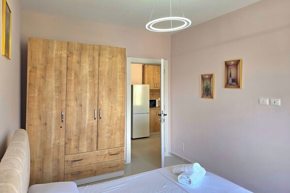 Une chambre avec une armoire en bois, un lit, une table de chevet et une vue sur la cuisine.