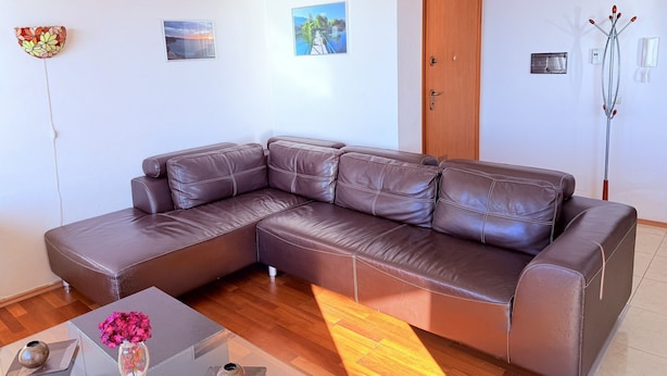 A brown leather sectional sofa, a glass coffee table with pink flowers, and two framed pictures on the wall. - Beachfront Apartment In Durres 072 (Durrës)