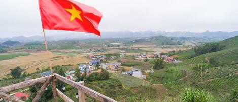 A flag on a wooden post overlooking a rural landscape with terraced fields and scattered houses.