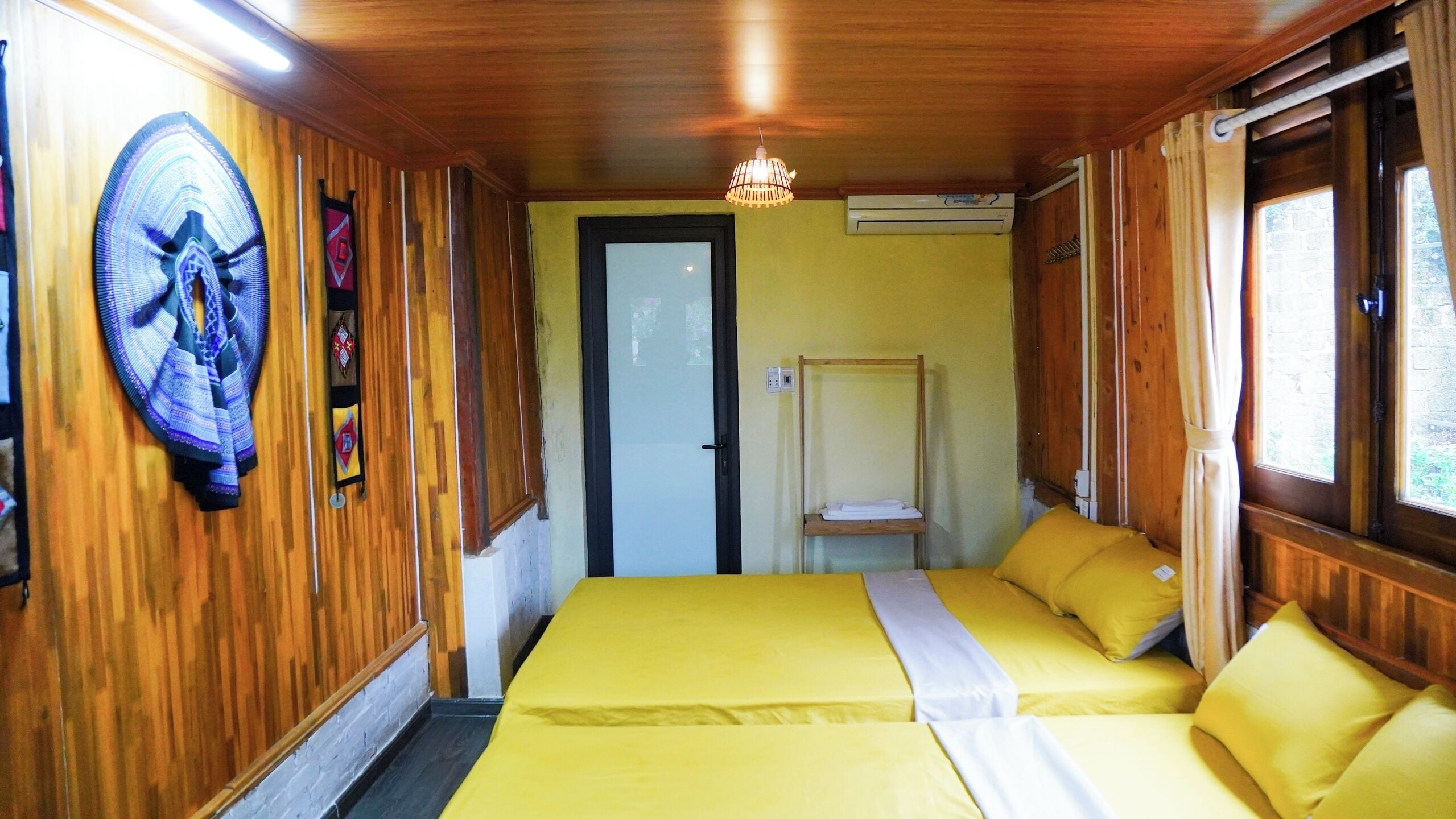 Una habitación con paredes de madera, una cama con ropa de cama amarilla, un ventilador y una puerta.