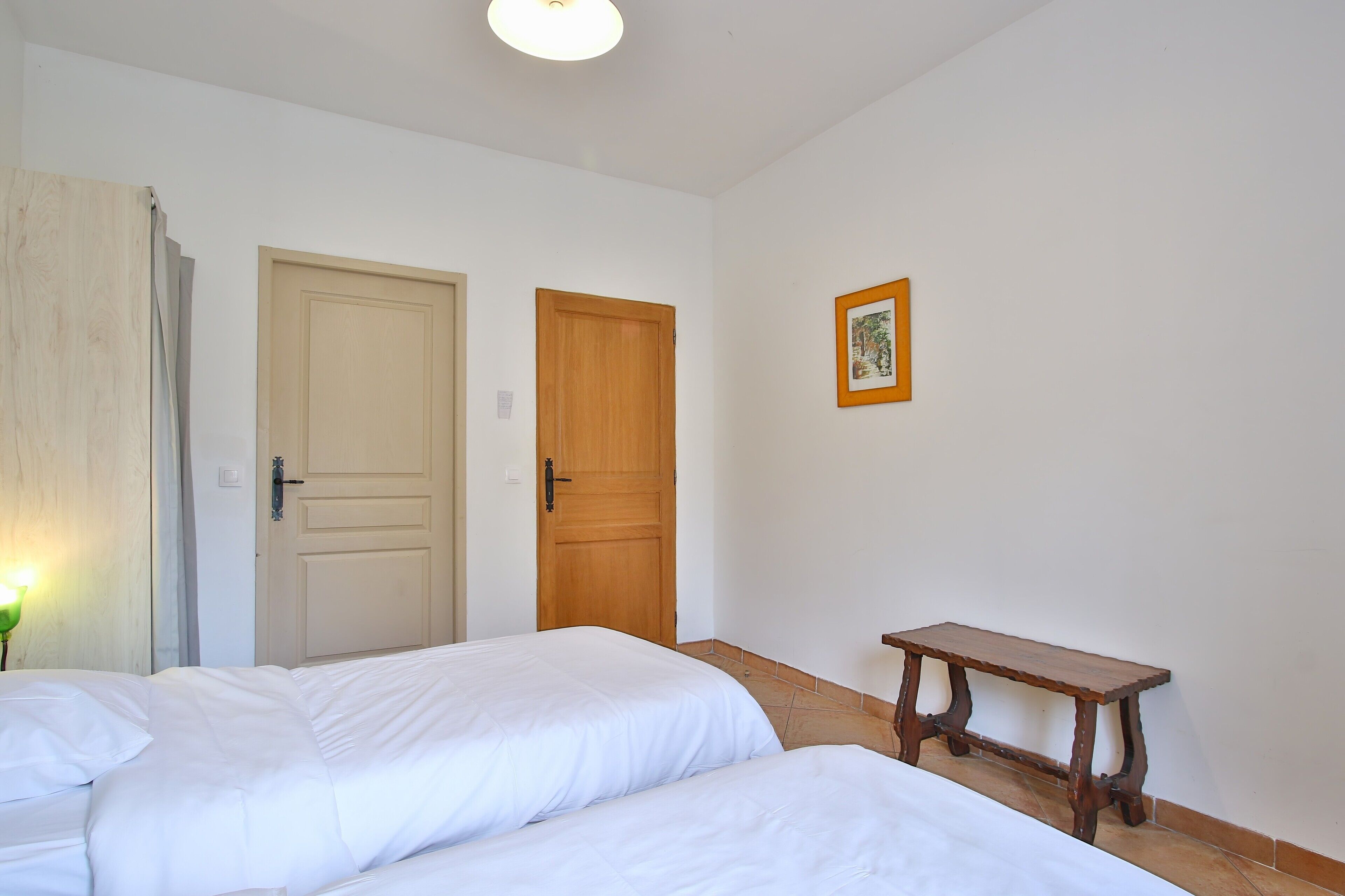 Ein Zimmer mit zwei Betten, einer Holztür, einem kleinen Tisch und einem gerahmten Bild an der Wand.