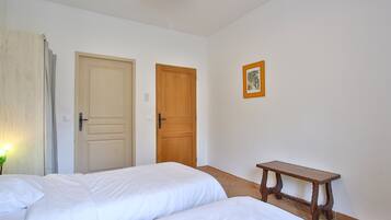 Ein Zimmer mit zwei Betten, einer Holztür, einem kleinen Tisch und einem gerahmten Bild an der Wand.