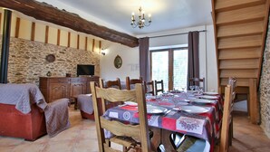 A dining area with a table set for four, wooden chairs, a stone wall, a television, and a chandelier.