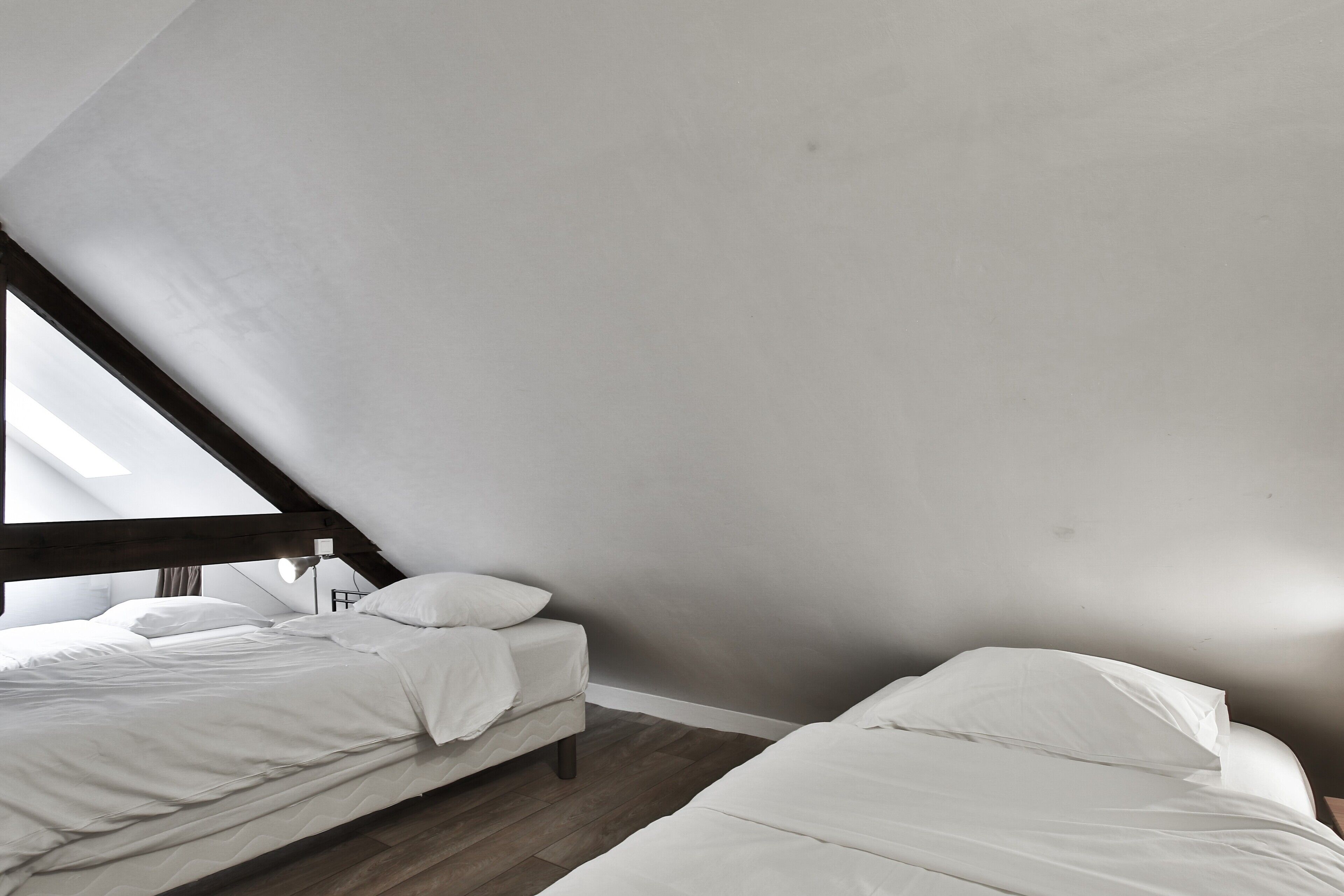 Een kamer met twee bedden, houten vloeren en een schuine kap.