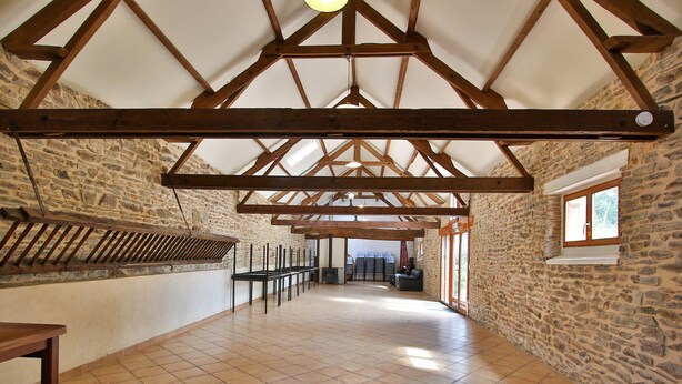 A spacious interior with exposed wooden beams, stone walls, and a tiled floor.
