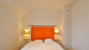 A single bed with an orange headboard, two bedside lamps, and a small table with a lamp.