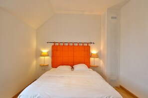 A single bed with an orange headboard, two bedside lamps, and a small table with a lamp.