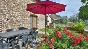A stone building with a patio table and chairs, a red umbrella, and red flowers.