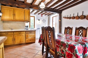 Una cocina rústica con armarios de madera, salpicadero de azulejos y un comedor con mantel floral.