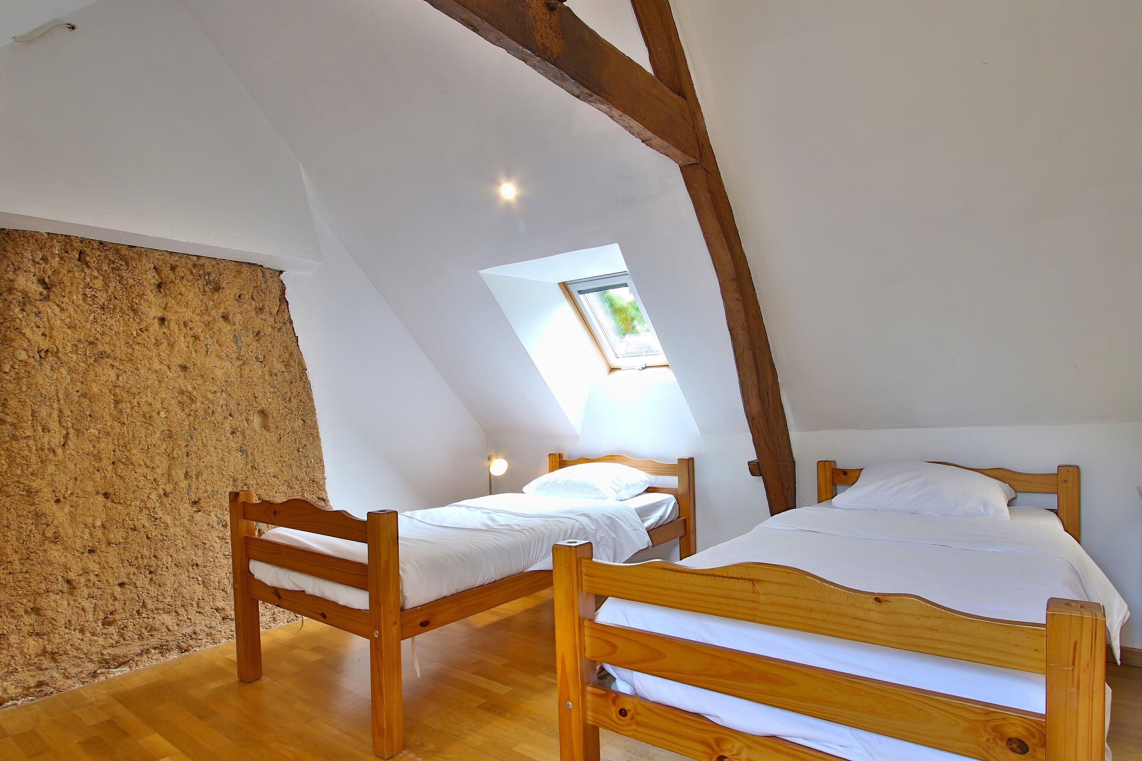 A room with two wooden beds, a sloped ceiling, and a skylight.