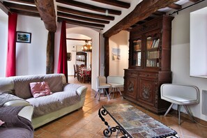 A living room with a sofa, a dining area with chairs, a cabinet with books, and a tiled floor.