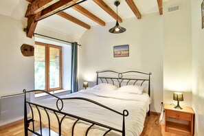 A bedroom with a bed, a window, a picture on the wall, and a nightstand with a lamp.