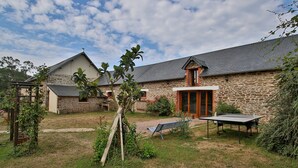 Un edificio in pietra con tetto spiovente, una pergola in legno e una panchina nel giardino.