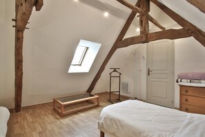 Une chambre avec un plafond en pente, une fenêtre, un lit, une commode et un radiateur.