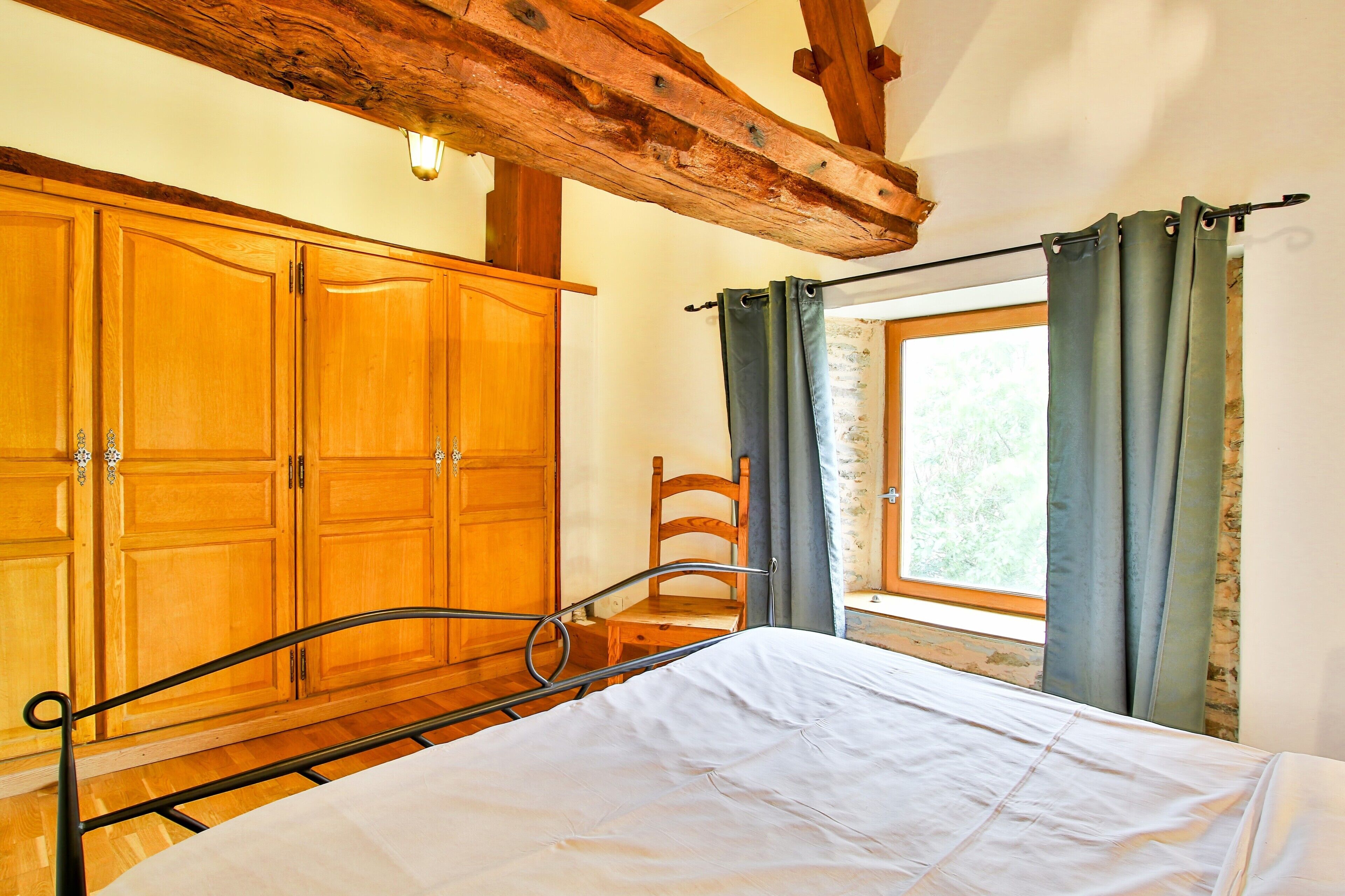 Un dormitorio con un armario de madera, estructura de cama de metal y ventana con cortinas.