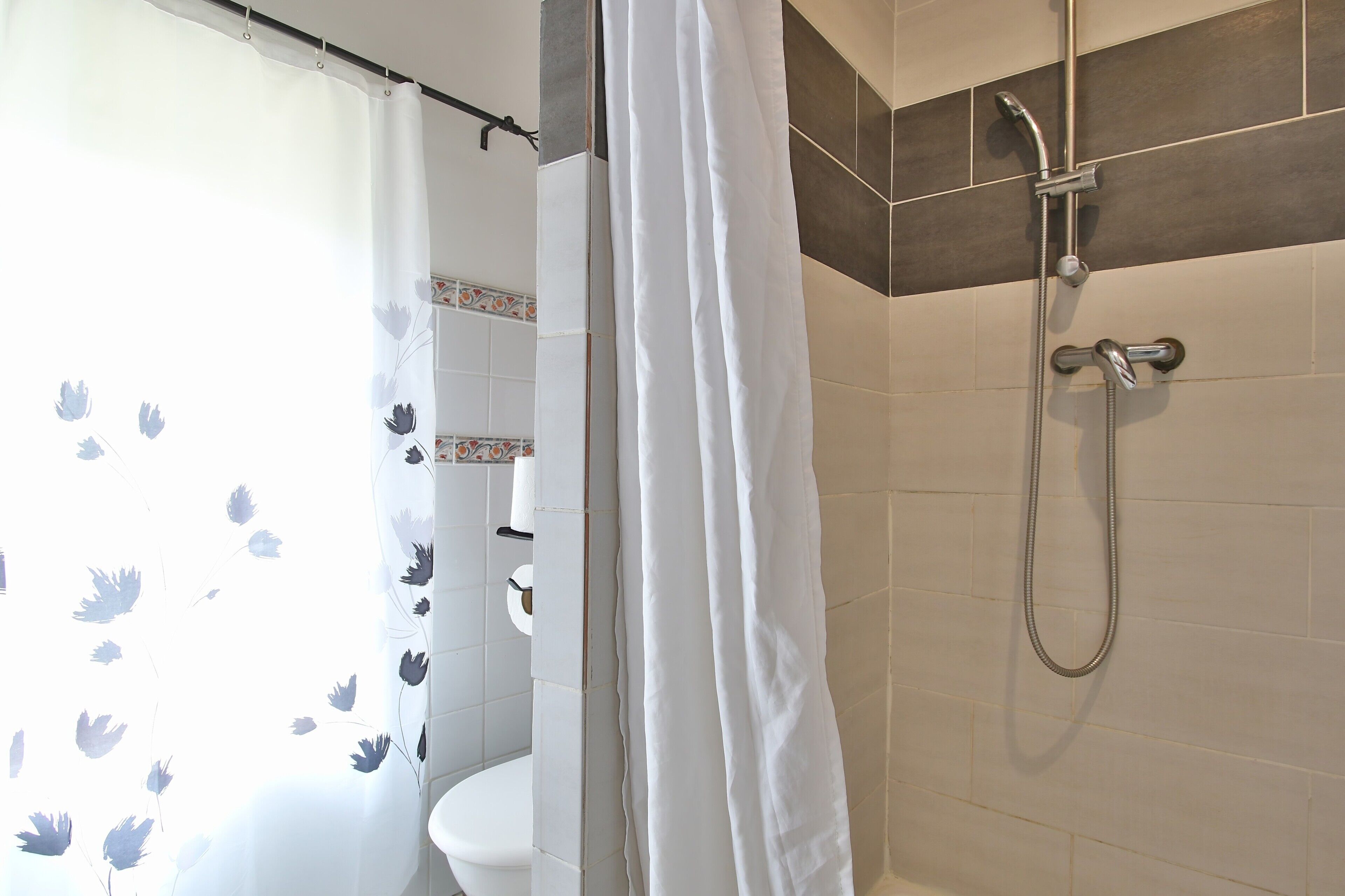 Un baño con ducha, inodoro y cortina estampada con motivos florales.