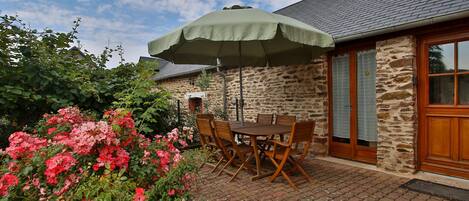 En terrasse med et bord og stole, en parasol, og en bygning af sten med en trädør.