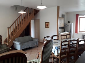 Zona pranzo con tavolo imbandito per quattro persone, divano, una scala e cucina sullo sfondo.