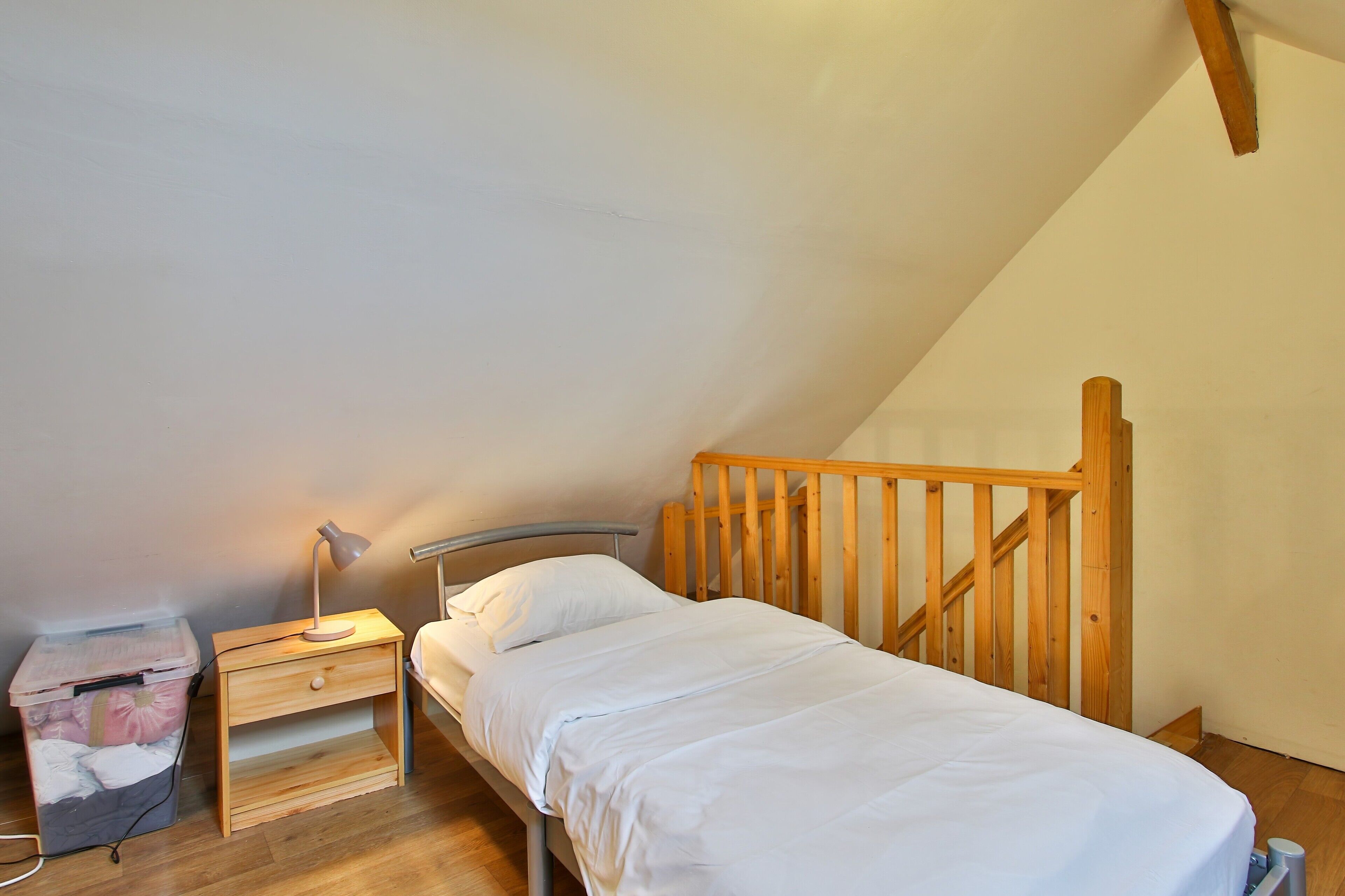 Een eenpersoonsbed met houten hoofdeinde in een kamer met schuine plafonds.