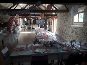 Un lungo tavolo da pranzo apparecchiato con decorazioni rosa e bianche, pareti in pietra e un rustico soffitto in legno.