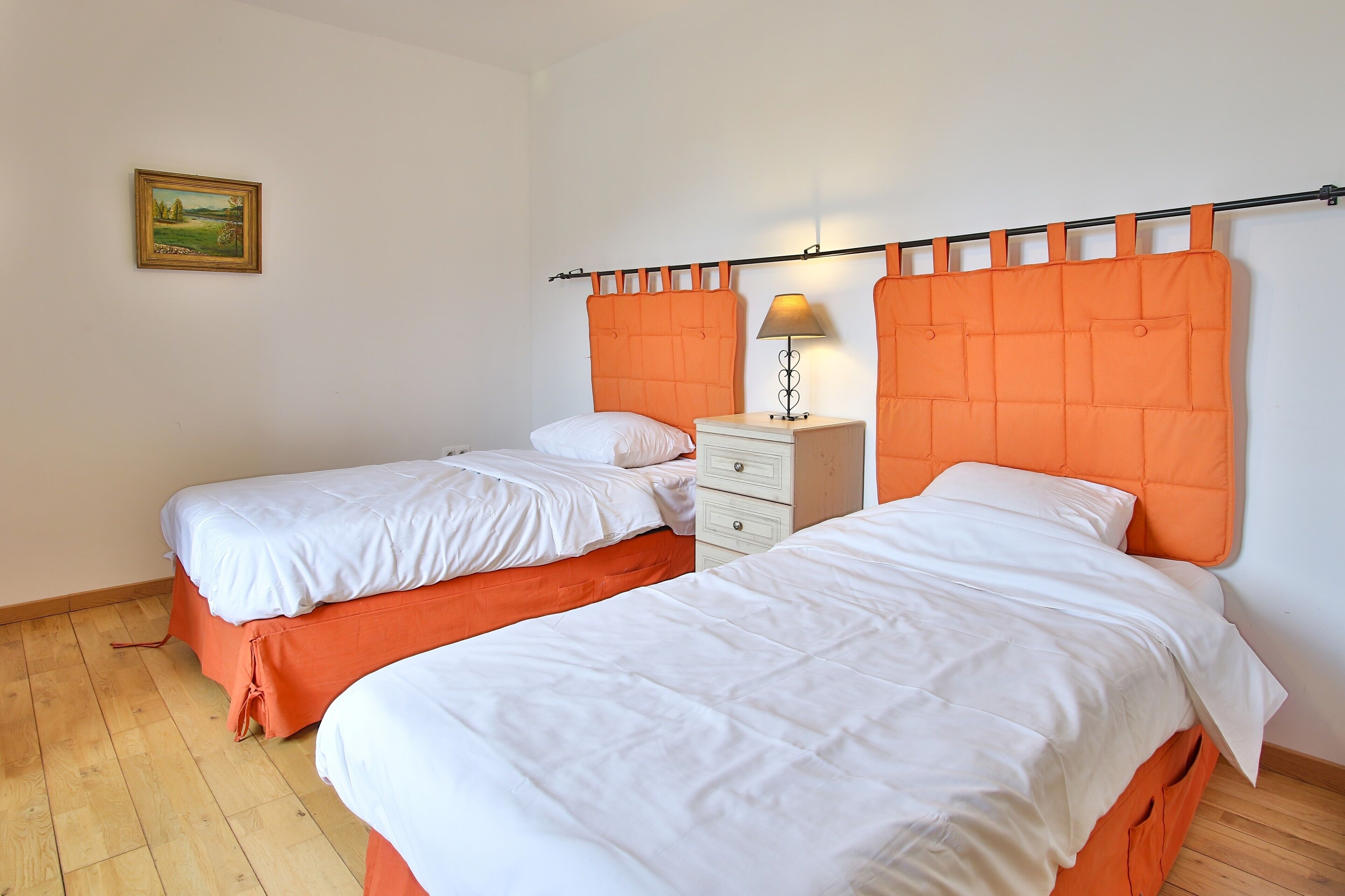 A room with two beds, a nightstand, a lamp, and a painting on the wall.