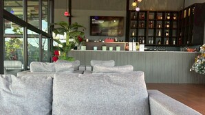 A modern living room with a grey sofa, a bar area with shelves of bottles, and a television mounted on the wall. - Rose Park Resort (Phang Khon)