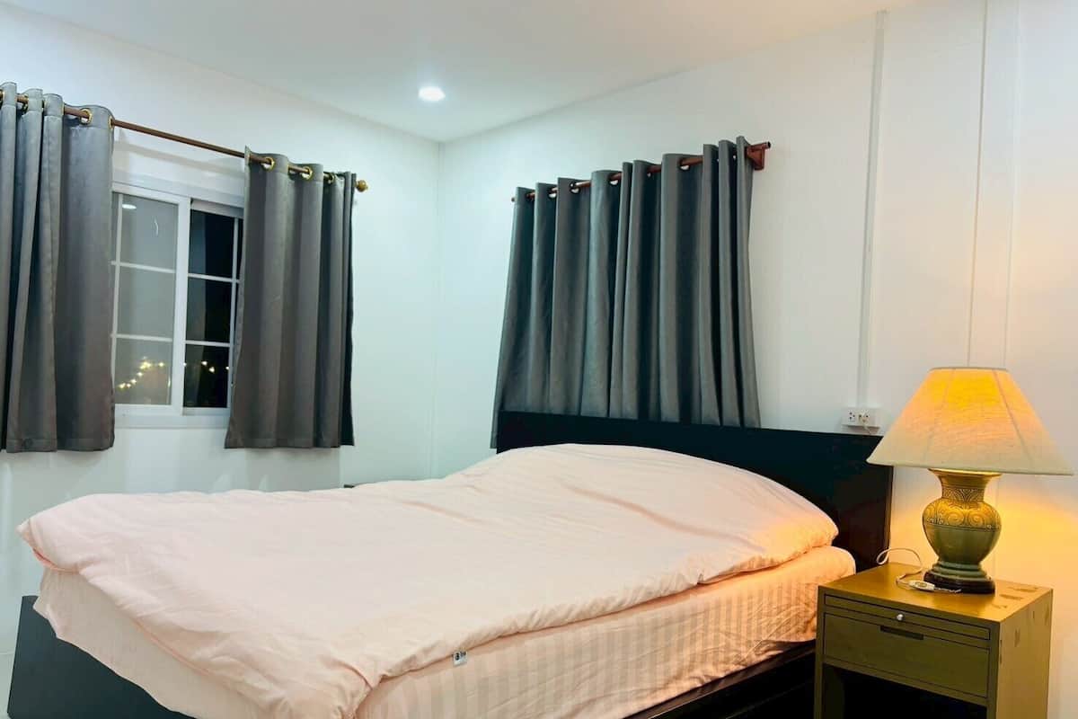 A bedroom with a bed, a nightstand, a lamp, and curtains.