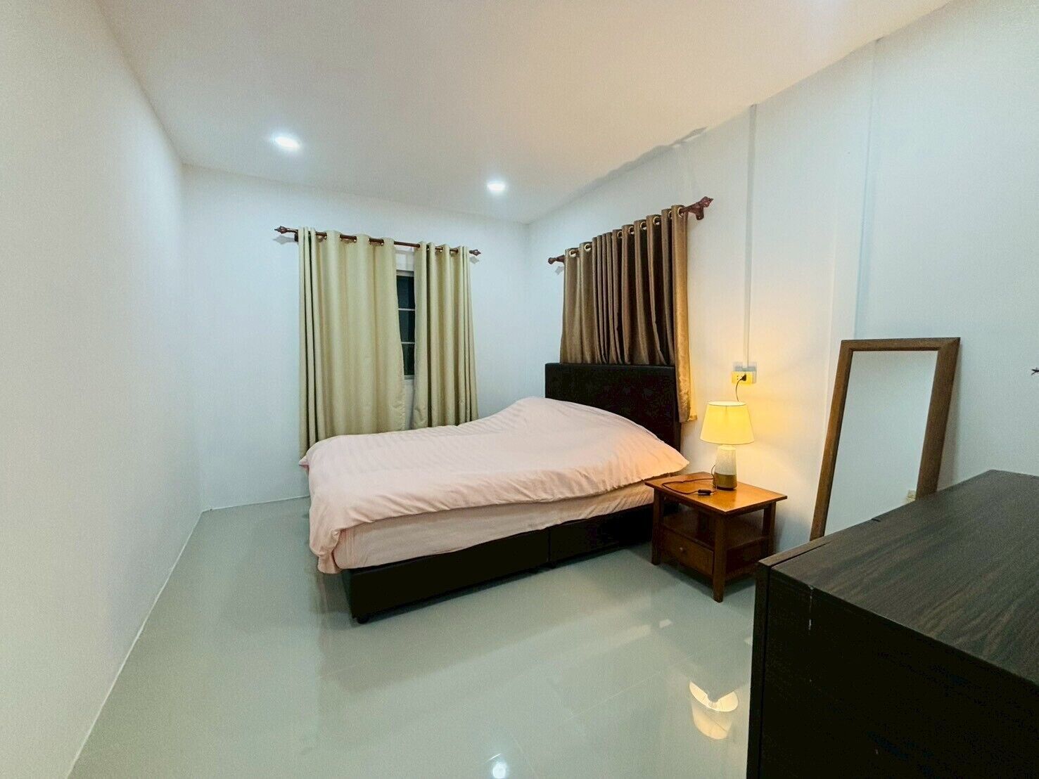 A modern bedroom with a bed, bedside table, lamp, and a mirror.