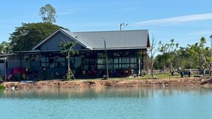 A building with a large windowed front, a metal roof, and a water body in front. - Rose Park Resort (Phang Khon)