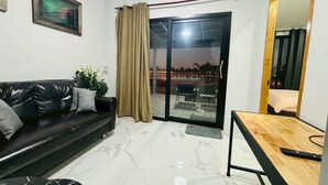 A modern living room with a black leather sofa, a wooden table, and a large sliding glass door leading to an outdoor area. - Rose Park Resort (Phang Khon)