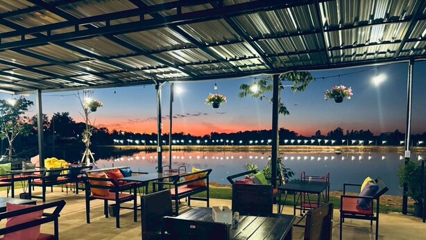 An outdoor seating area with tables and chairs, overlooking a body of water with a sunset view. - Rose Park Resort (Phang Khon)