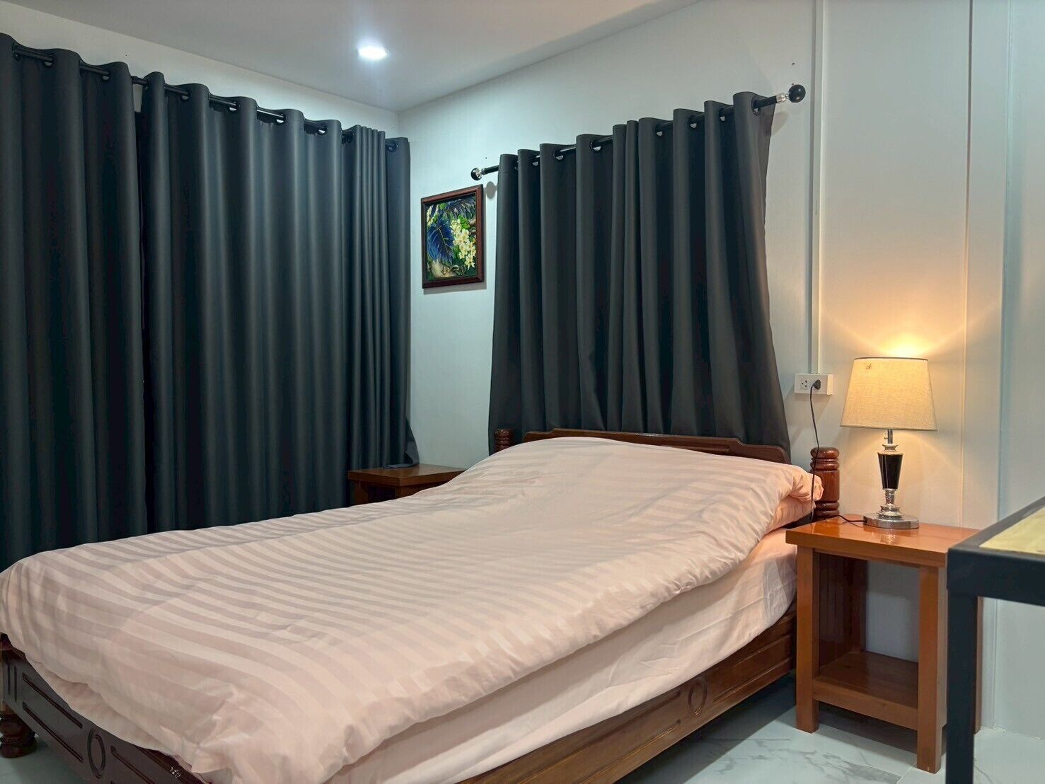 A bedroom with a bed, dark curtains, a bedside lamp, and a small table.