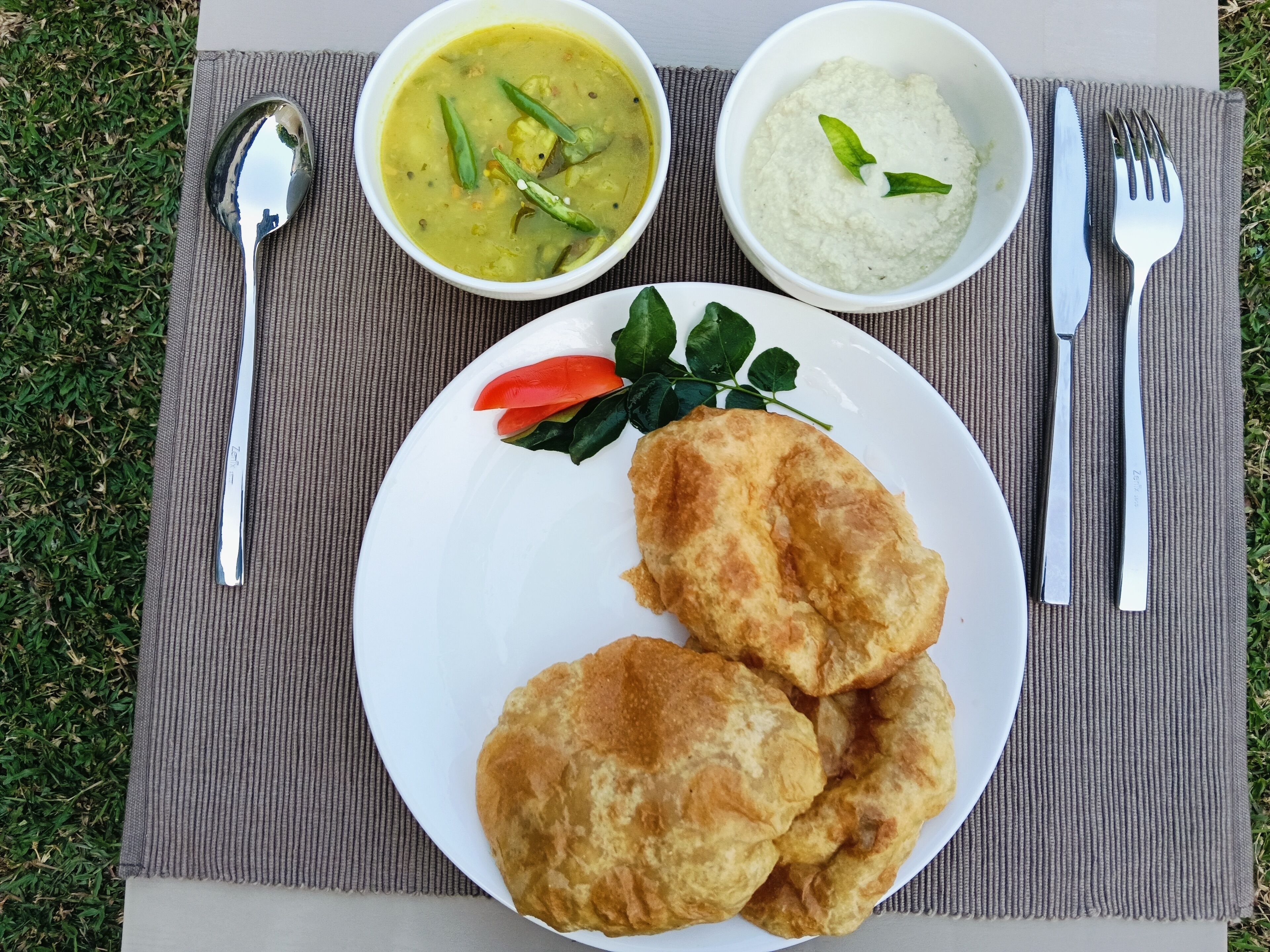 A plate with two fried items, a bowl of soup, and a bowl of rice on a mat.
