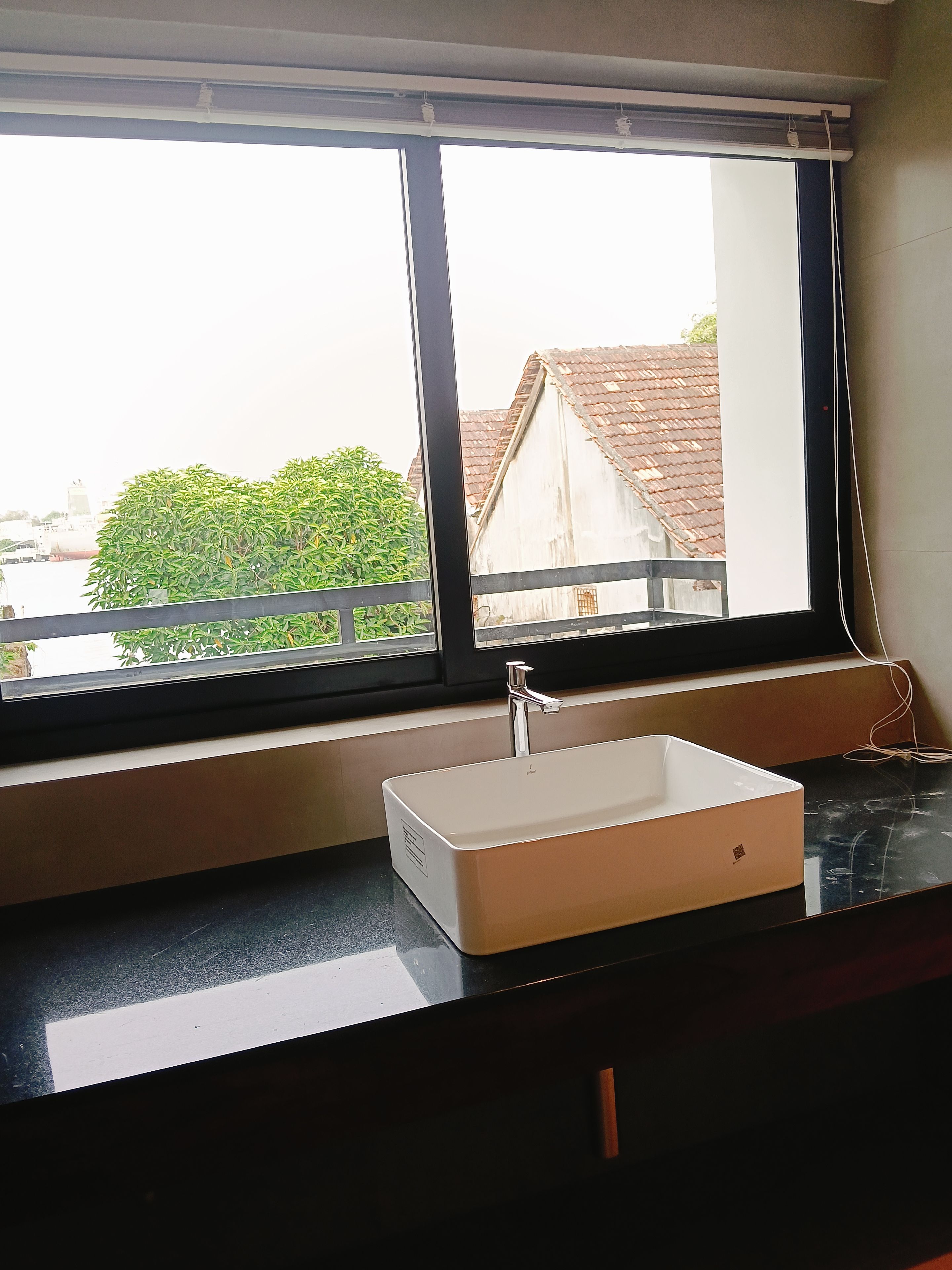 A bathroom with a window, a sink, and a view of buildings and greenery outside.
