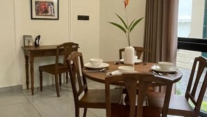 A dining area with a round wooden table, four chairs, and a vase with a single flower. There is a framed picture on the wall and a small table with a bowl and a sign. - CREEK HARBOUR KOCHI  (Kochi)