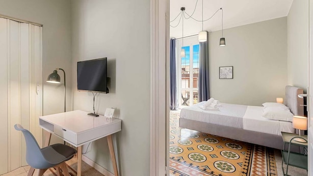 Ett hotellrum med en säng, ett skrivbord, en stol, en tv och utsikt över omgivningarna.