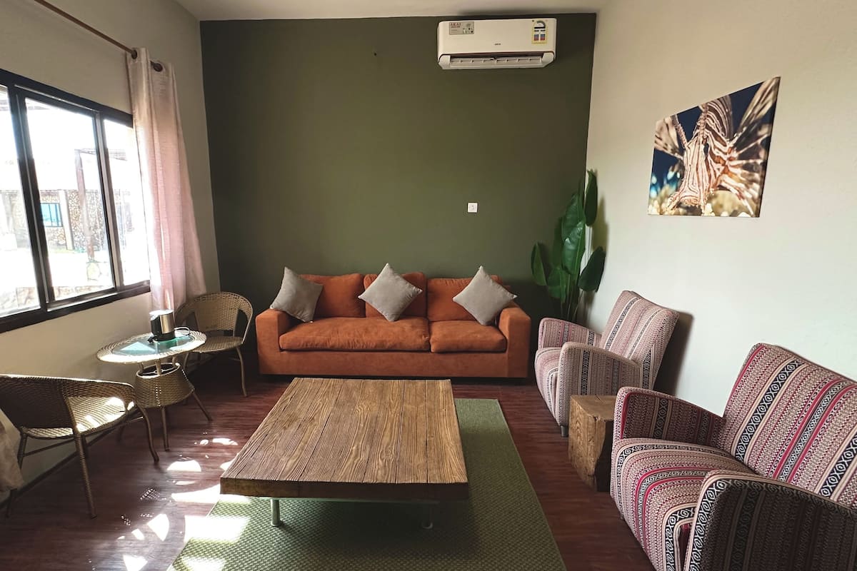 A living room with a sofa, a coffee table, a wicker chair, and a patterned armchair.