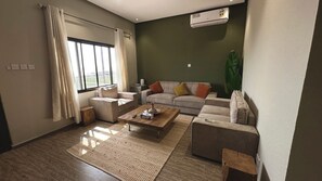 A living room with a sofa, coffee table, and a large window with curtains. - Roushan Resort  (Mirbat)