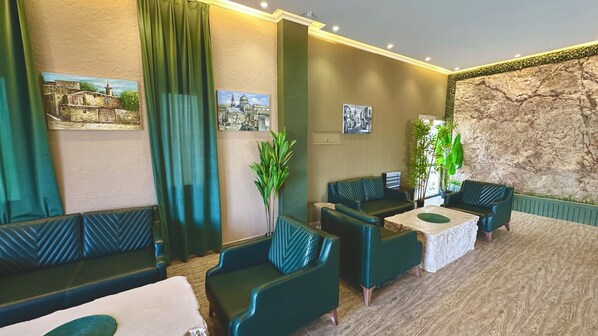 A hotel lobby with green upholstered seating, a stone accent wall, and framed artwork on the walls. - Roushan Resort (Mirbat)