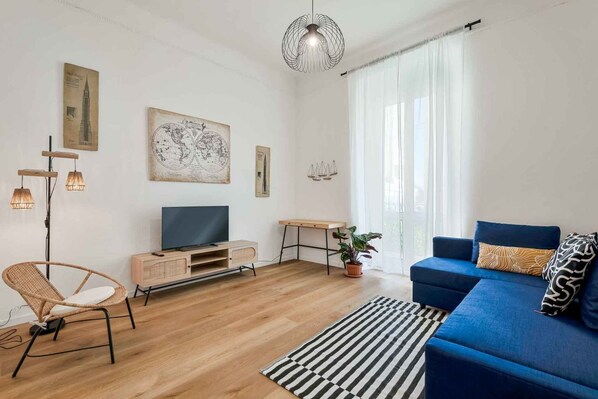 Ein modernes Wohnzimmer mit einem blauen Sofa, Holzboden, einem Fernseher, einem Korbsessel und einer Weltkarte als Wandbild.