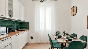 Moderni keittiö, jossa on valkoiset kaapit, vihreä välitila ja ruokailutila, jossa on puinen pöytä ja vihreät tuolit.