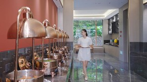 A modern hotel lobby with a long counter displaying multiple copper pots, a person in a white dress, and a large window with a view of greenery. - Langyun Garden Hotel (Guilin)
