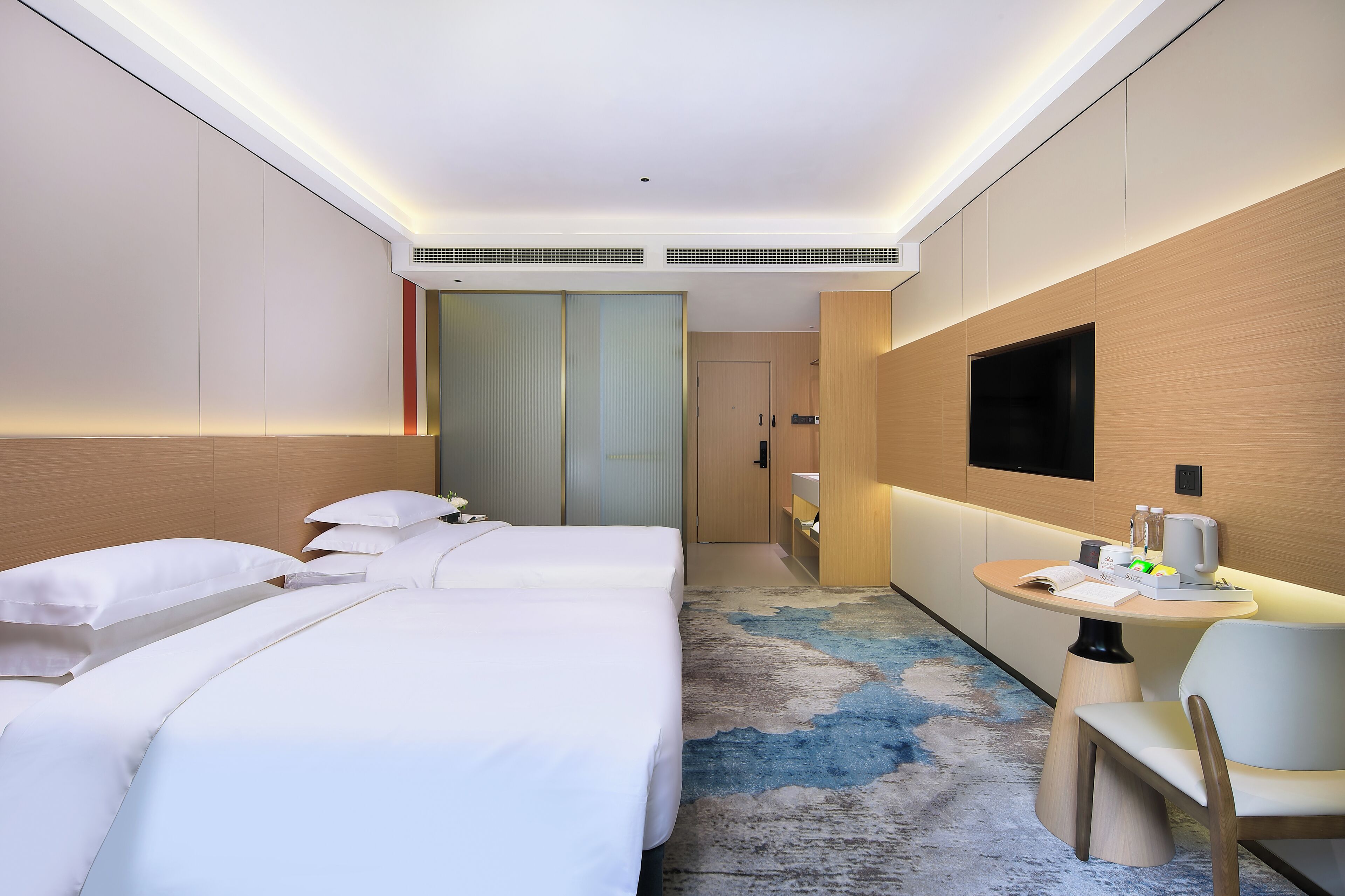 Een hotelkamer met twee bedden, een kleine tafel met een stoel, een aan de muur bevestigde televisie en een badkamer die door een deur zichtbaar is.