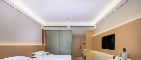 Een hotelkamer met twee bedden, een kleine tafel met een stoel, een aan de muur bevestigde televisie en een badkamer die door een deur zichtbaar is.