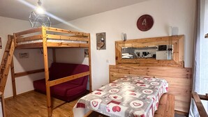 A bunk bed with a red bedspread, a wooden desk with a chair, a mirror, and a wall clock. - Apartment "La Cabane" in Chamrousse, Private Terrace, Ski-in/Ski-out (Chamrousse)