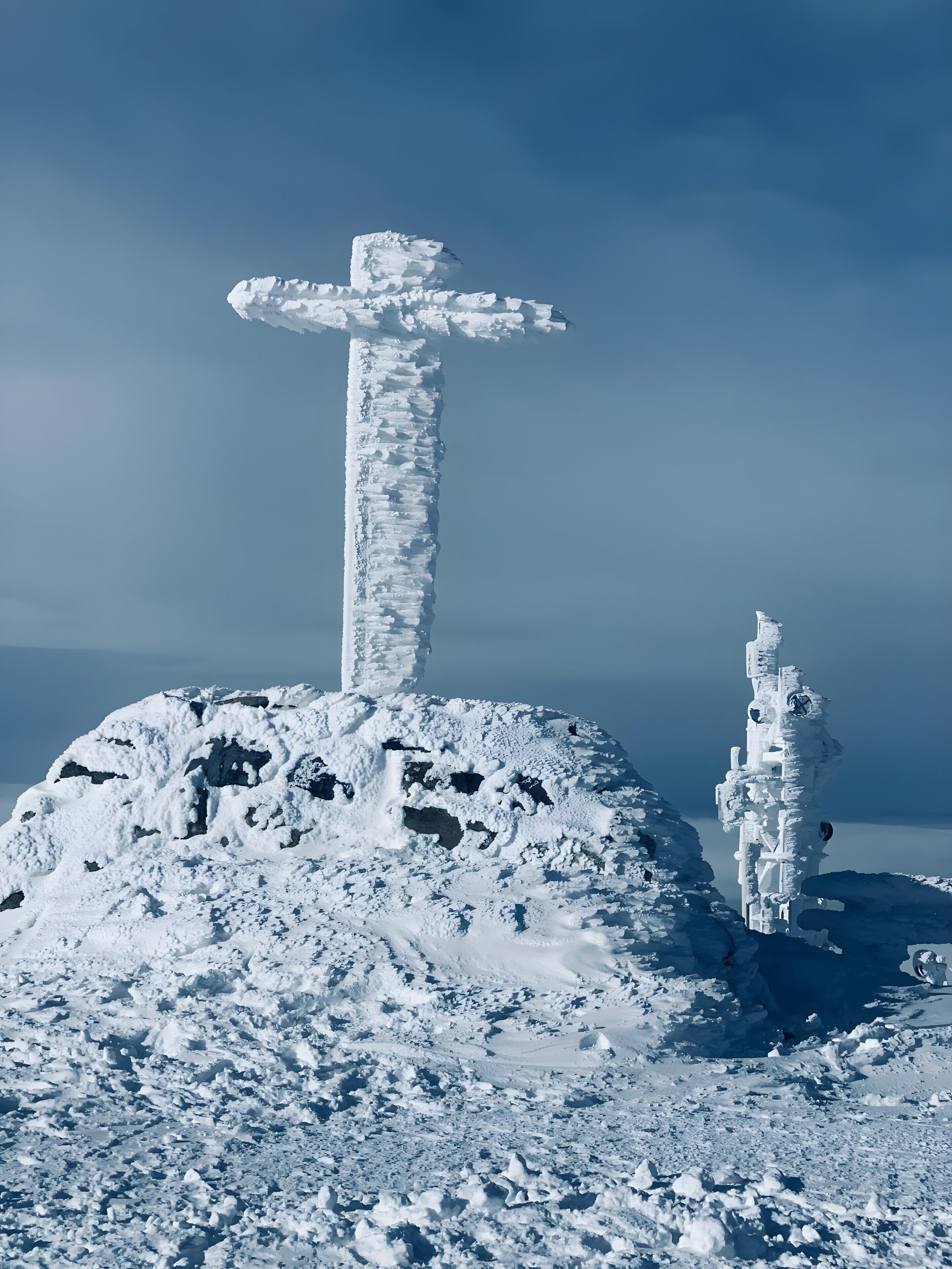 Una cruz cubierta de nieve en una colina bajo un cielo despejado.